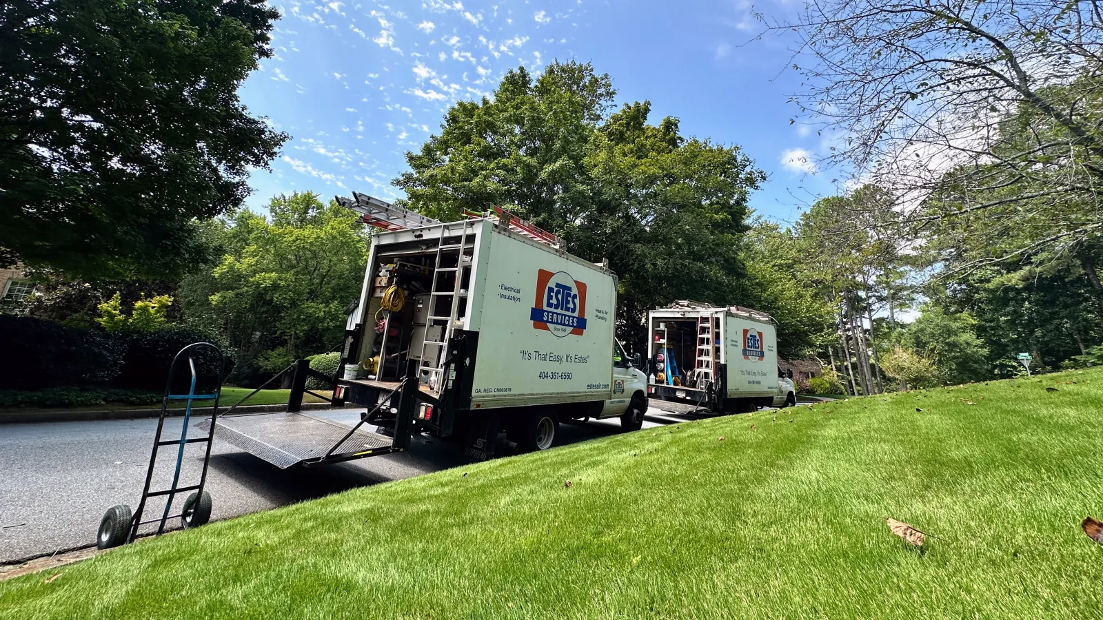 Two Estes Services trucks parked on a residential street with open rear doors and equipment visible on a sunny day.