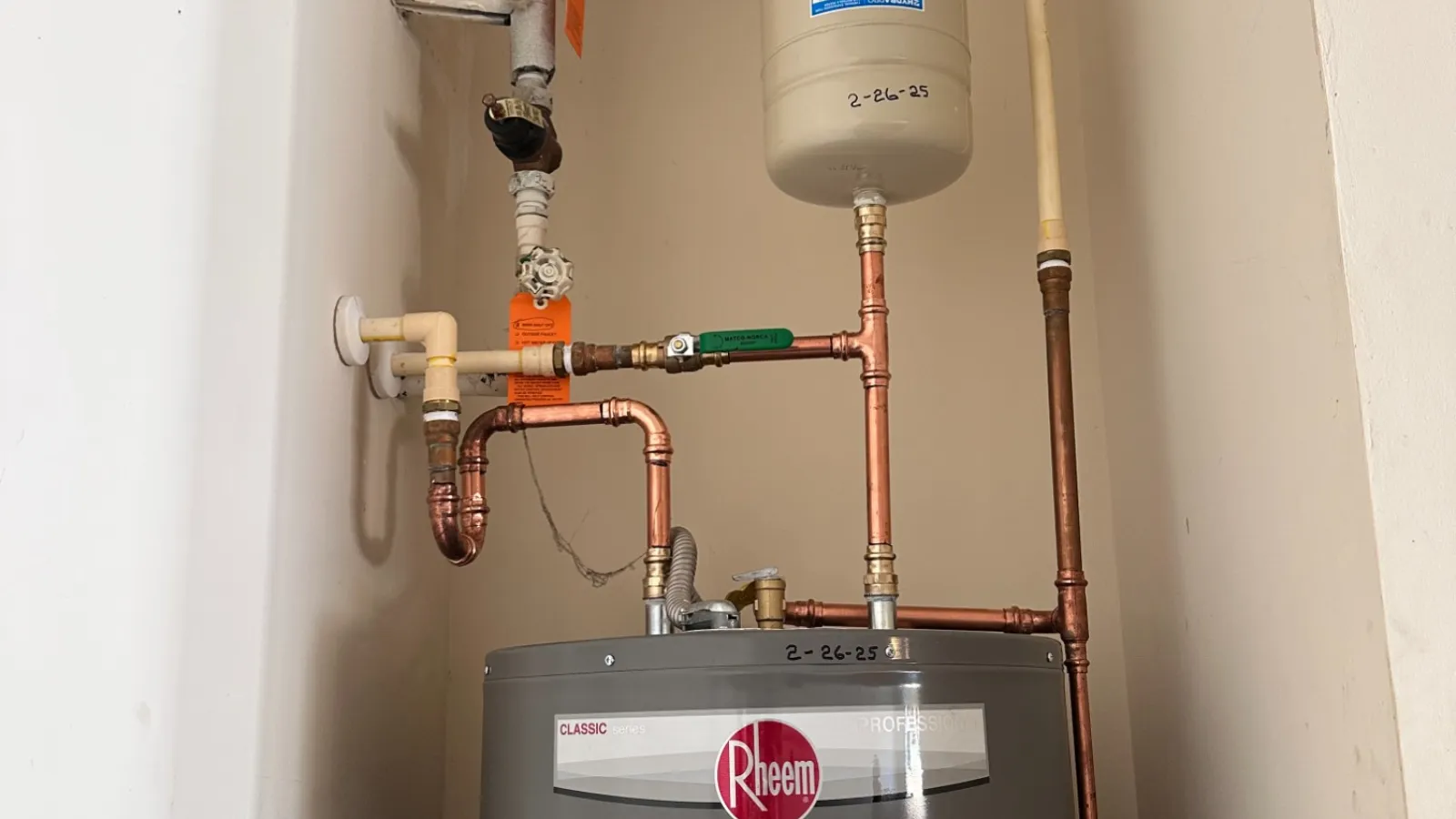 Rheem water heater with copper piping and an expansion tank installed in a small utility closet.
