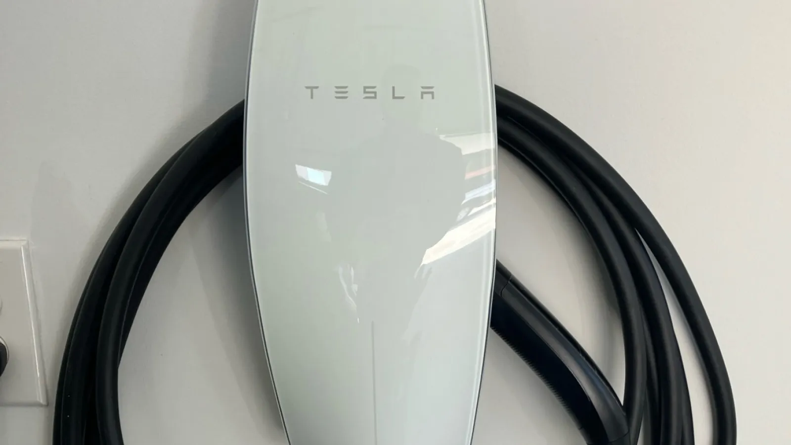 Estes Servicesinstalled Tesla electric vehicle charging cable with sleek white charger and coiled black cord on white surface