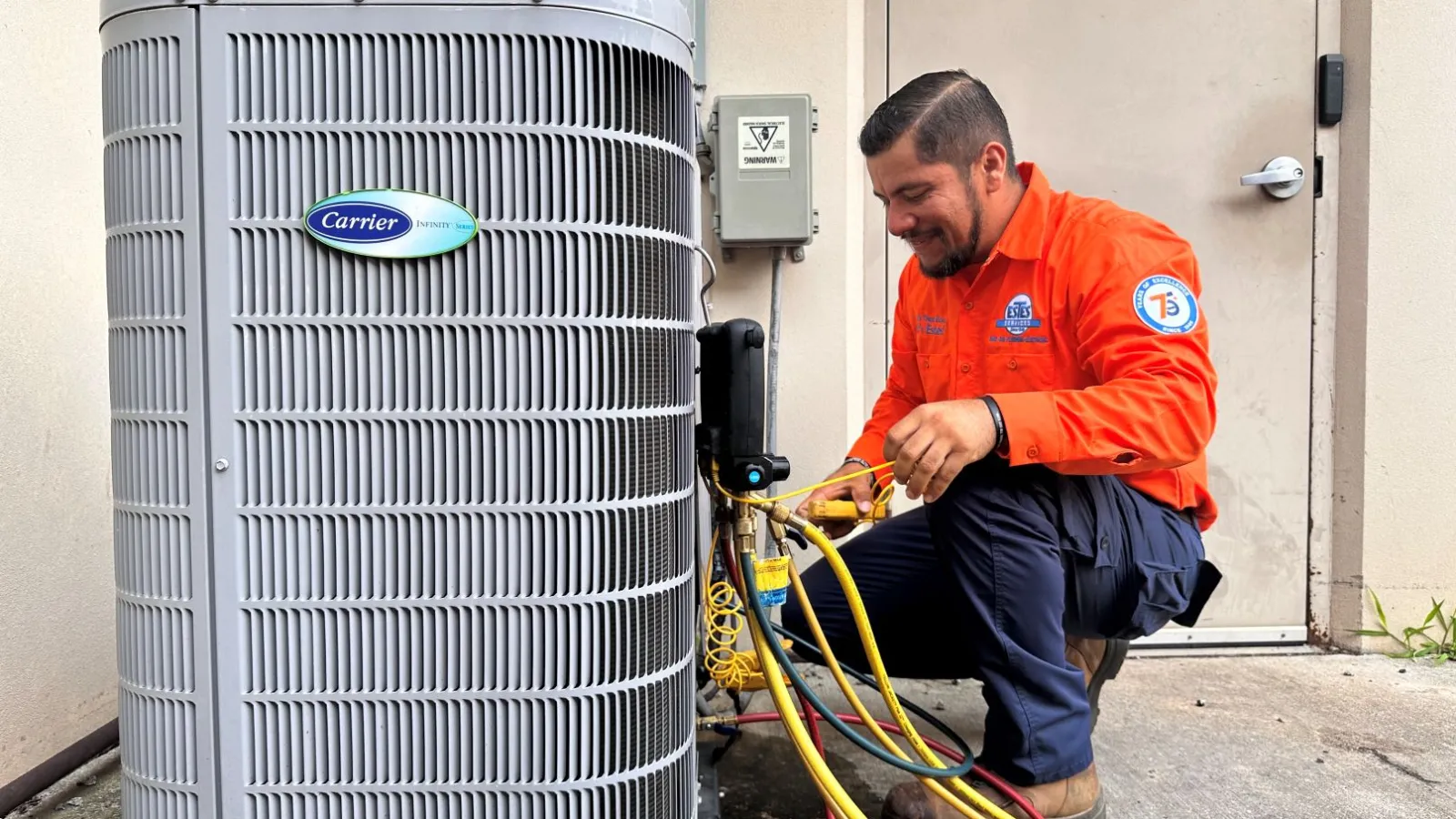 Technician in Estes Services uniform servicing a Carrier heat pump unit outdoors with diagnostic hoses attached