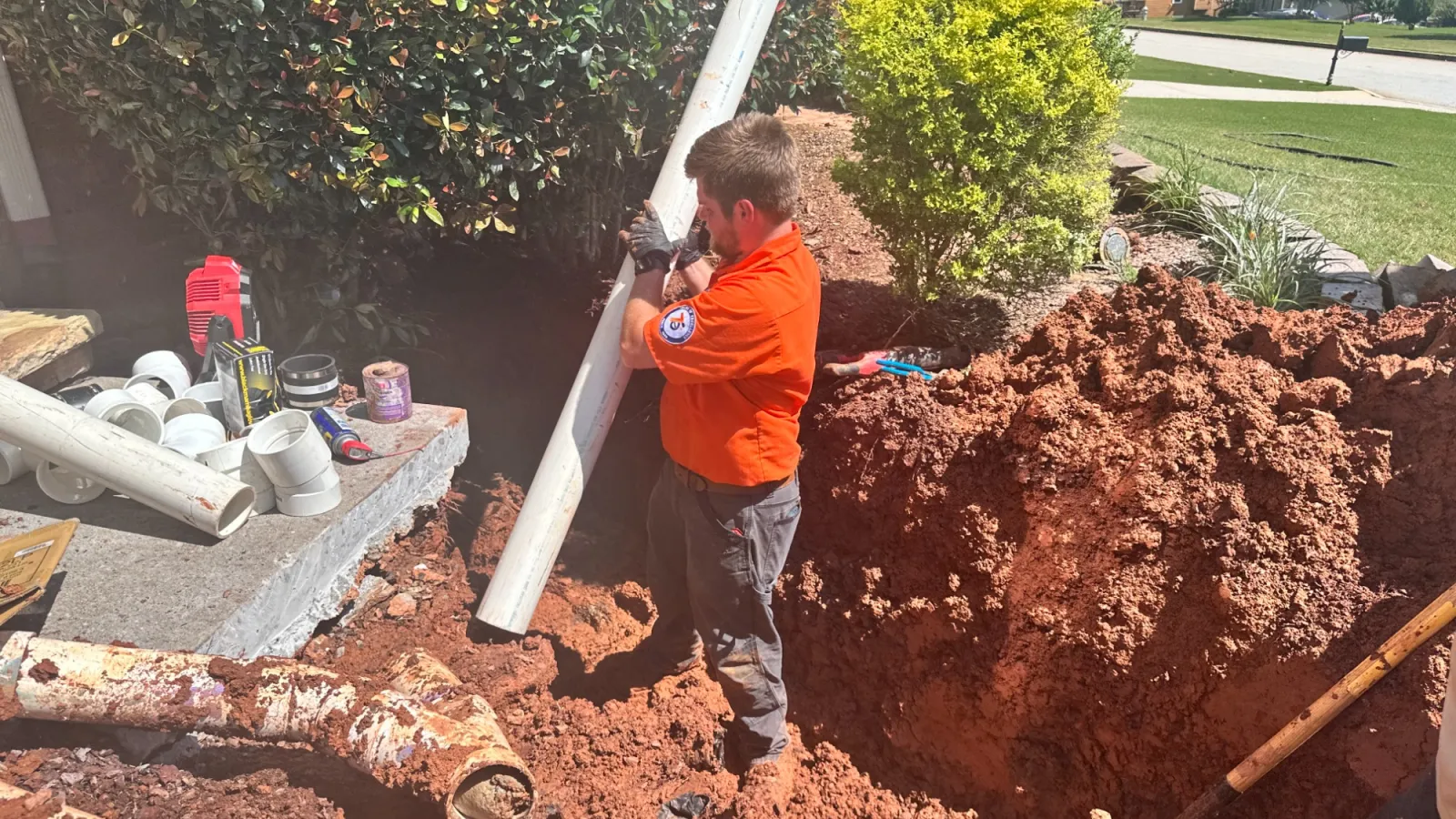Estes plumber in orange Estes uniform reparing a sewer line in residential yard.