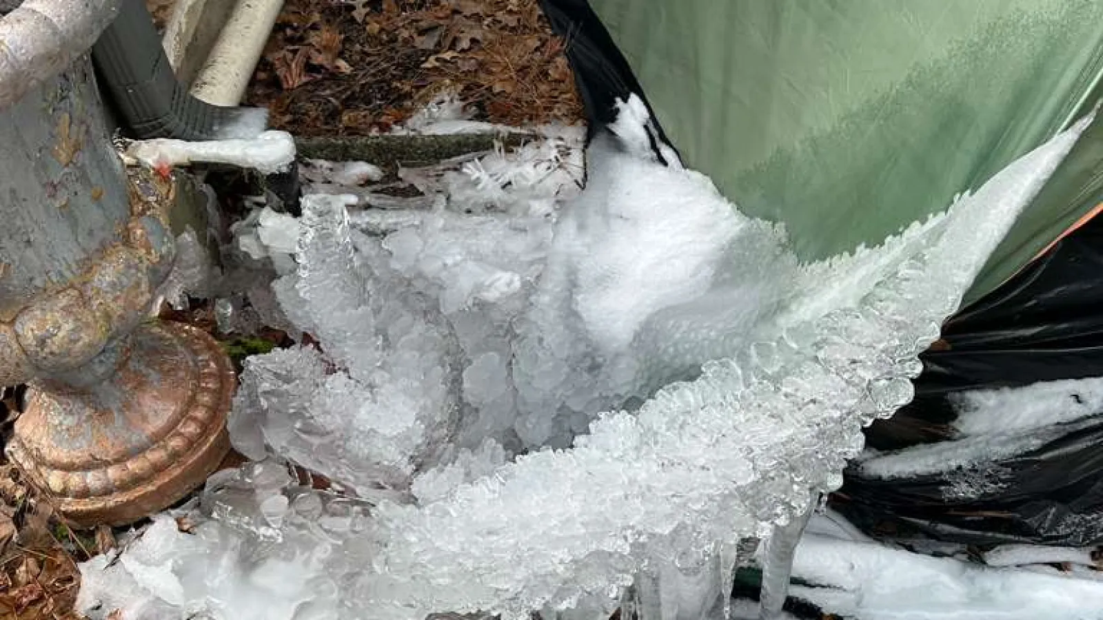 Frozen pipe around green tent and outdoor area with pipes and fallen leaves in wintertime.