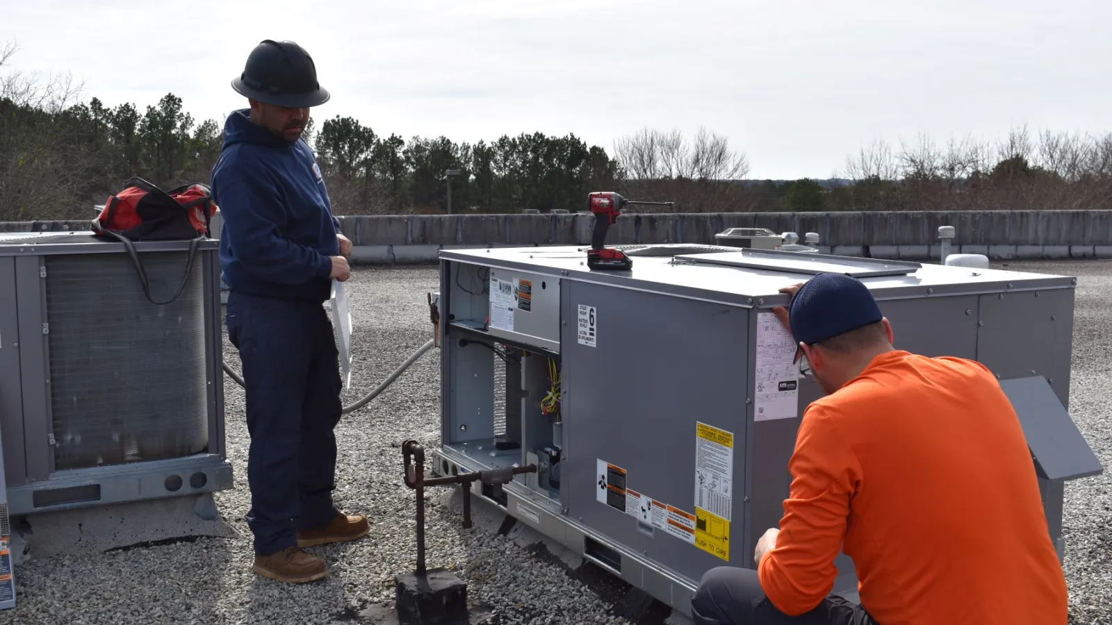 Two technicians Estes Commercial Services inspecting and repairing rooftop HVAC units on a commercial building.