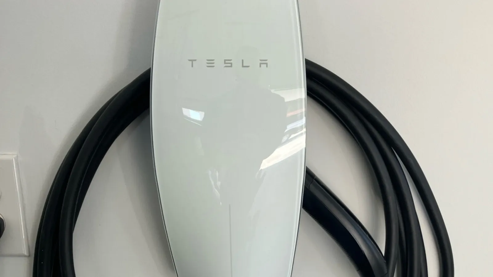 Tesla Wall Connector electric vehicle charging station installed by Estes Services with coiled black cable on white wall.