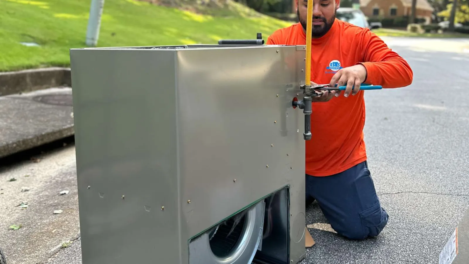Estes Technician working on Carrier HVAC unit with Estes Services logo promoting heat, air, plumbing, and electrical services.