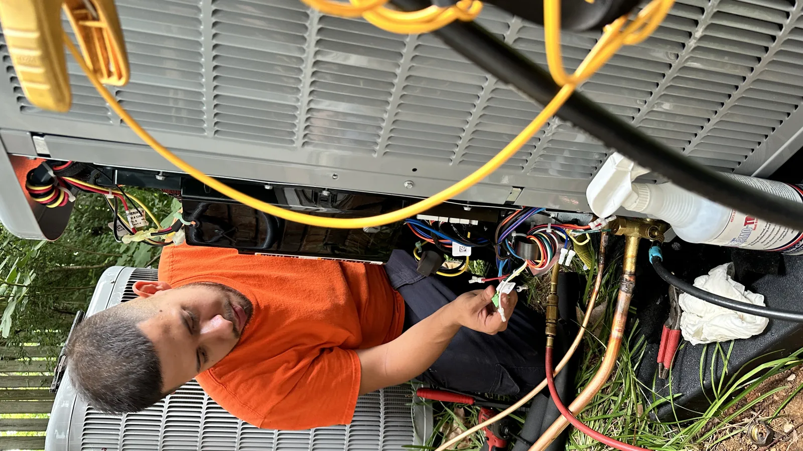 Estes Installer in orange uniform installing a Carrier Heat Pump with wiring and tools around.