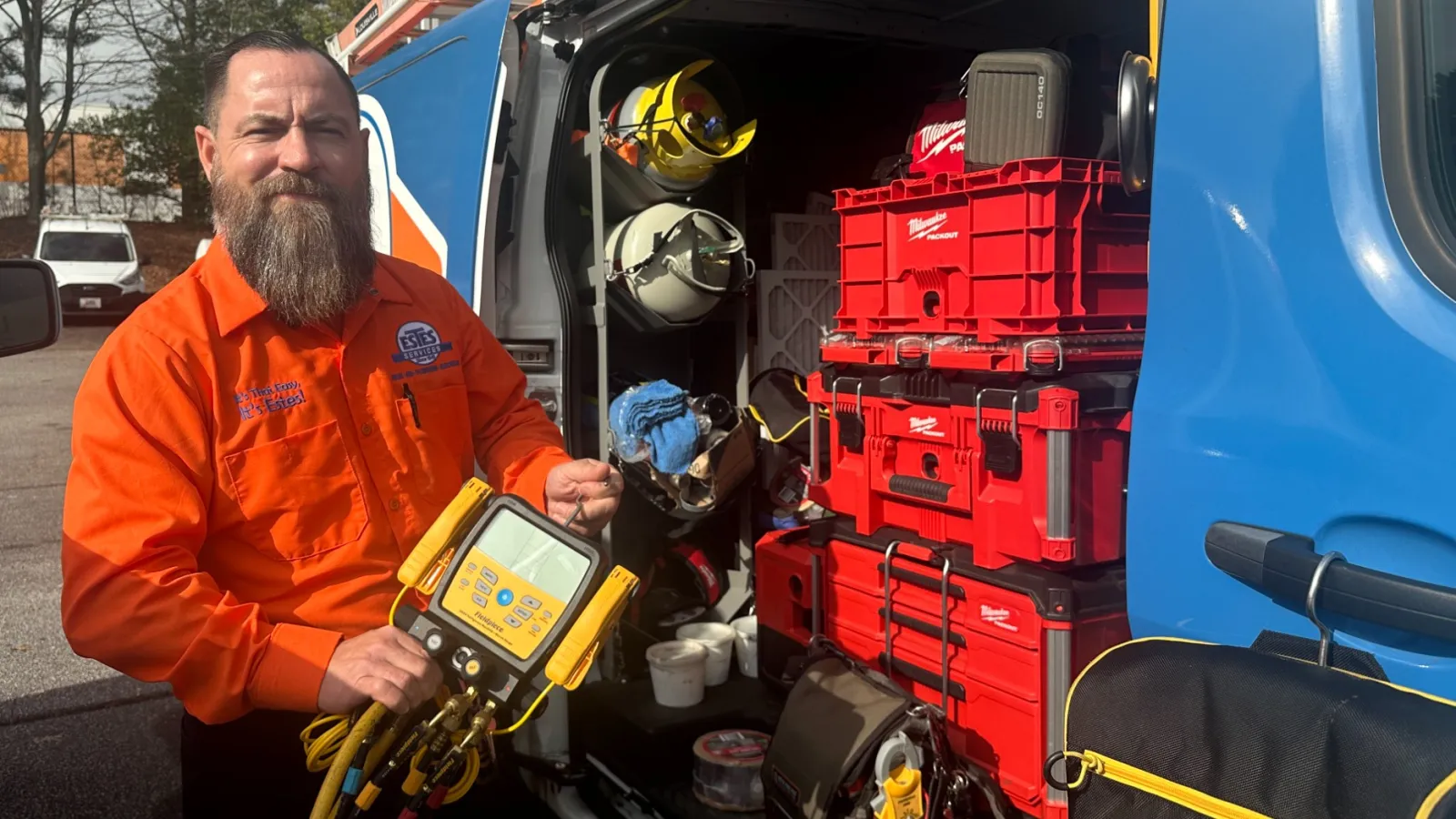 Jeremy, Estes Air Technician in orange uniform holding HVAC diagnostic tool beside organized van with red toolboxes and equipment.