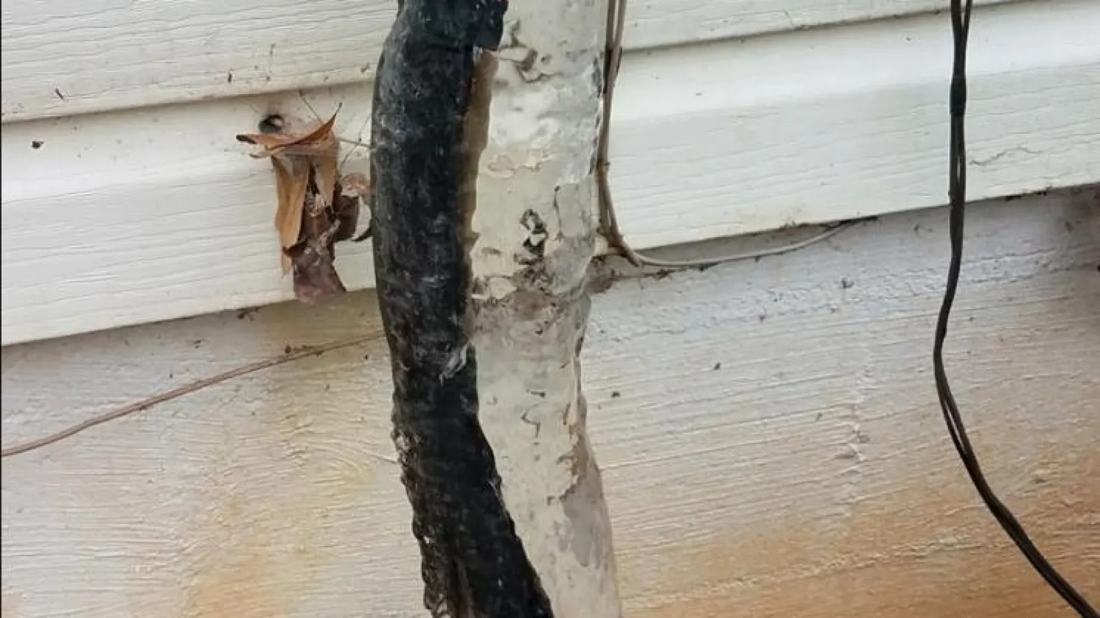 Frozen and damaged outdoor cables with ice buildup against a house exterior wall in winter