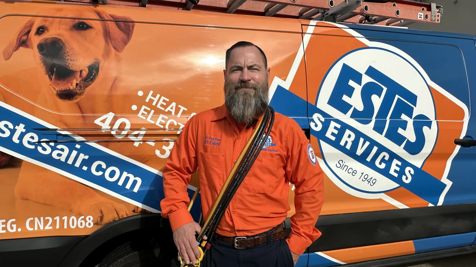 Need AC? Estes Technician in orange uniform with tools stands in front of orange and blue Estes Services van with dog image.