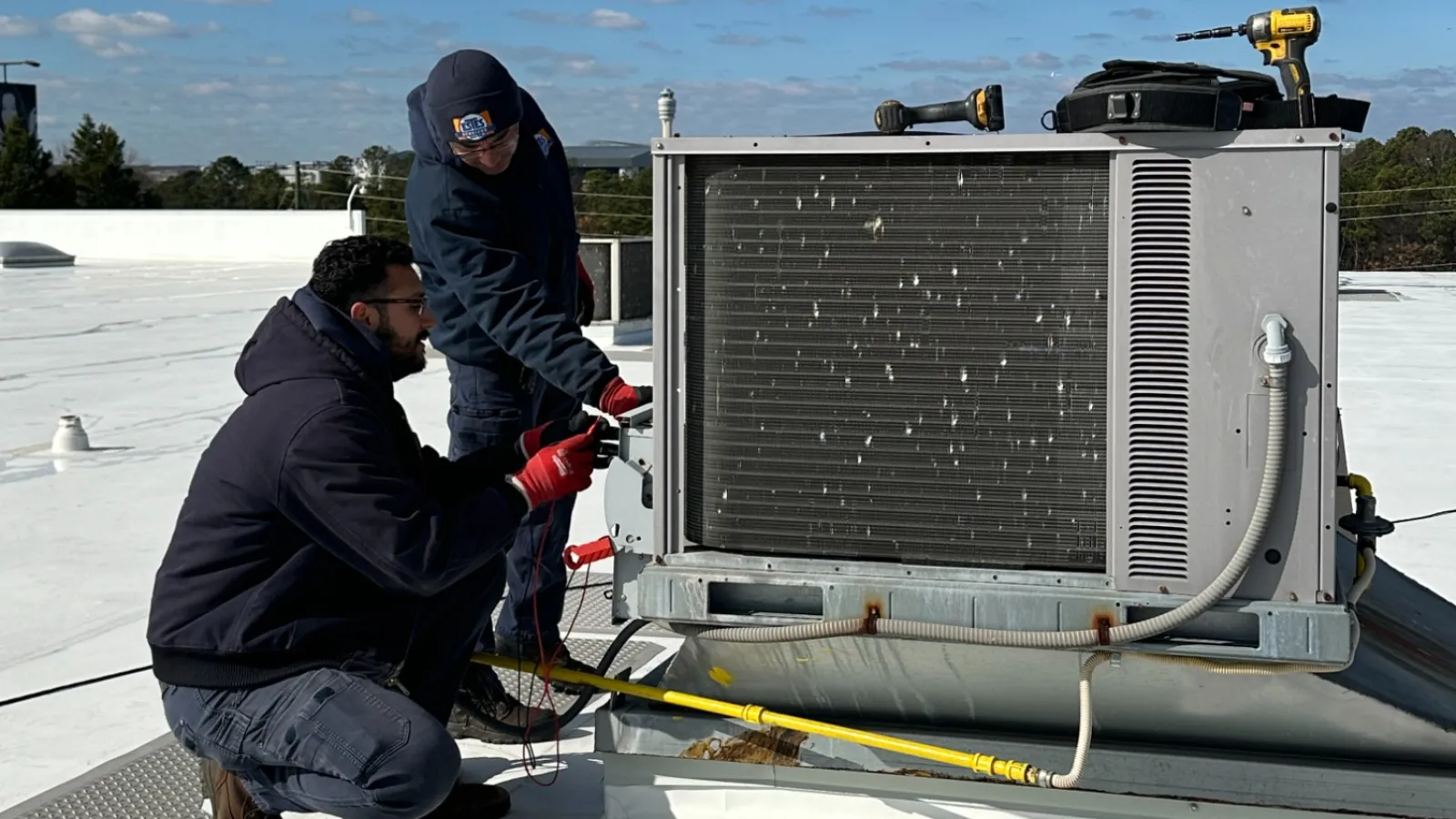 Two technicians working on rooftop HVAC unit under a clear blue sky during daytime maintenance