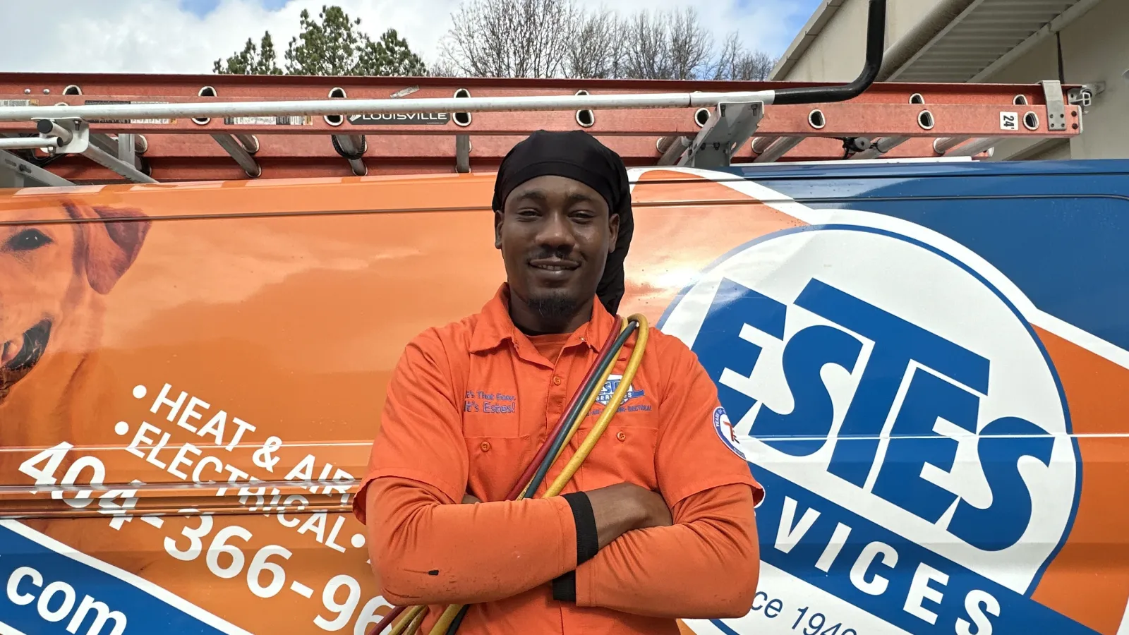 Smiling Estes Tech near you in orange uniform holding equipment hoses in front of Estes Services truck with ladder