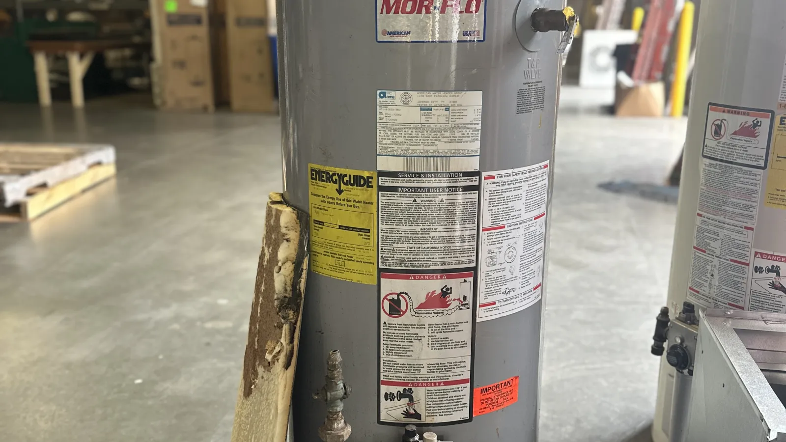 Water heater Old with labels and insulation panel leaning against it in a warehouse.