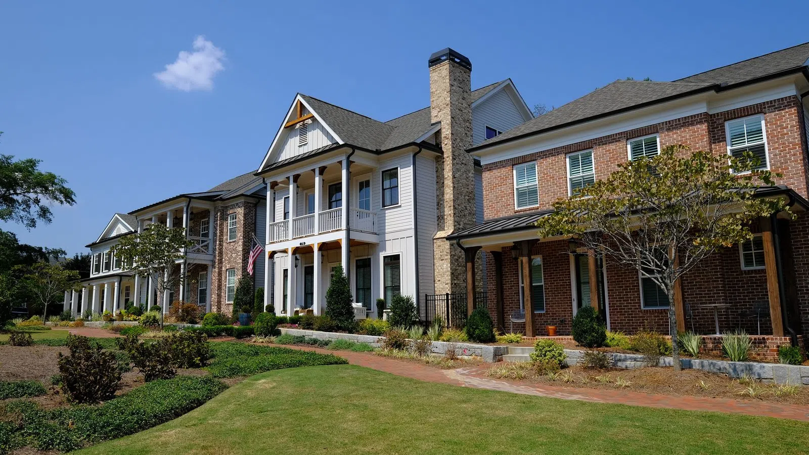 Row of modern suburban houses with well-maintained lawns and clear blue sky background.