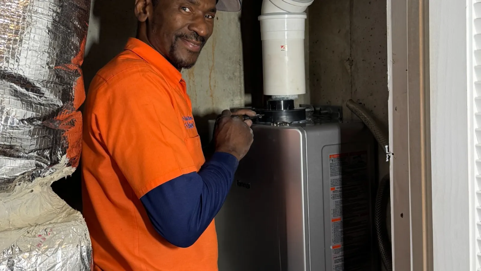 Estes Plumber in orange shirt uniform installing a home water heater in Atlanta