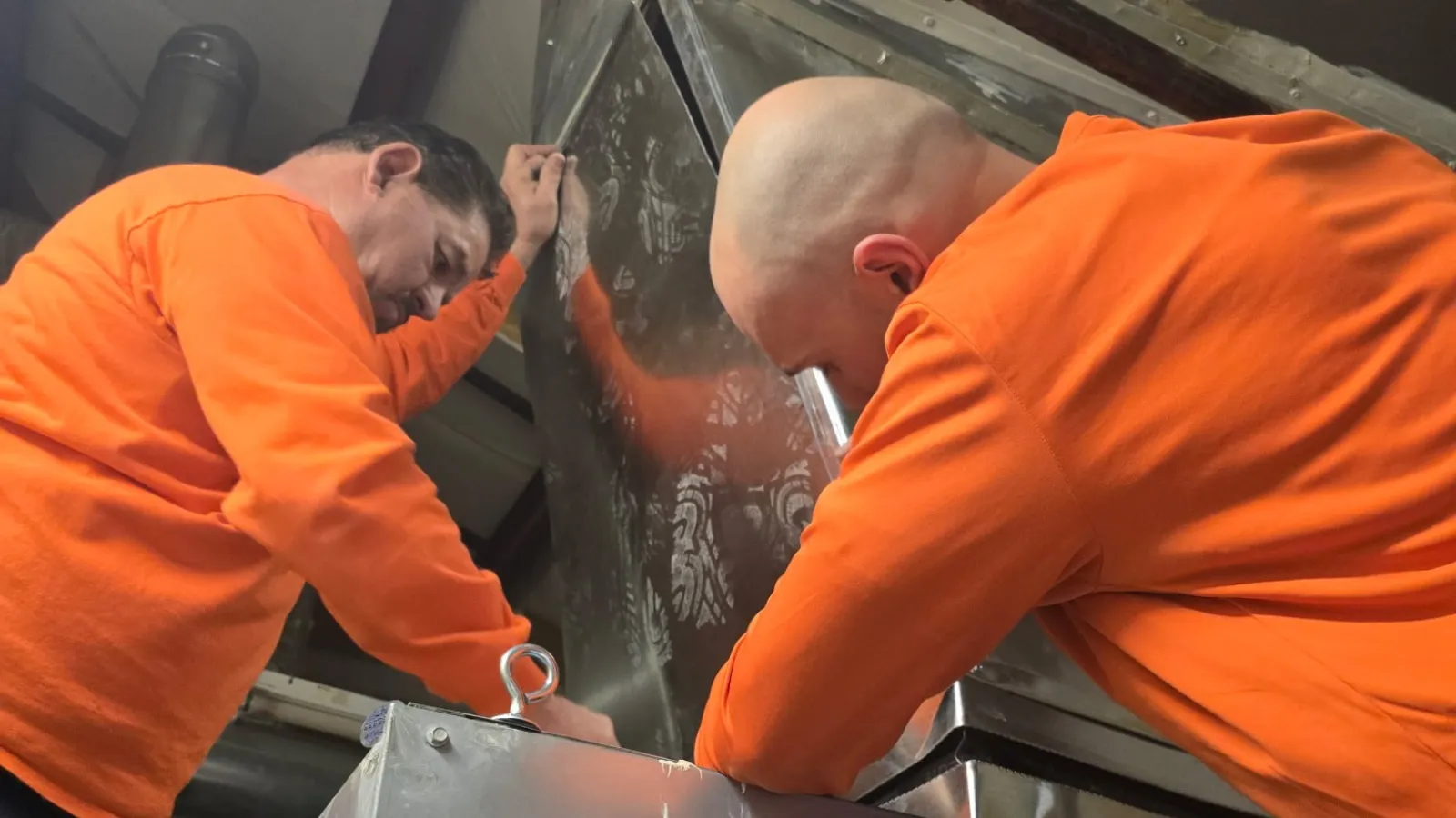 Two Estes Services technicians in orange uniform installing HVAC equipment inside a school in Atlanta