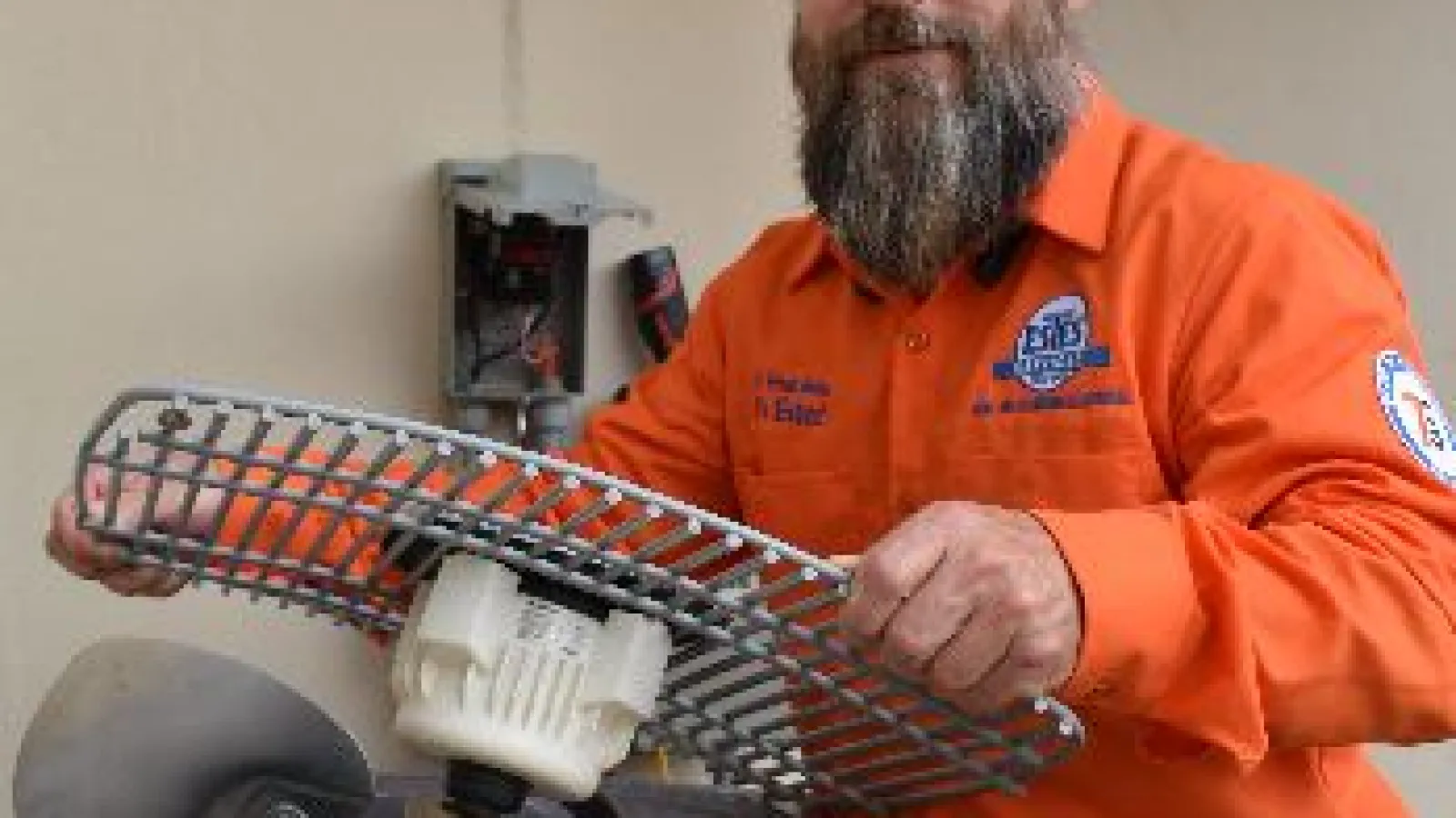 Technician in orange shirt repairing an outdoor HVAC unit fan assembly by removing the protective grill.