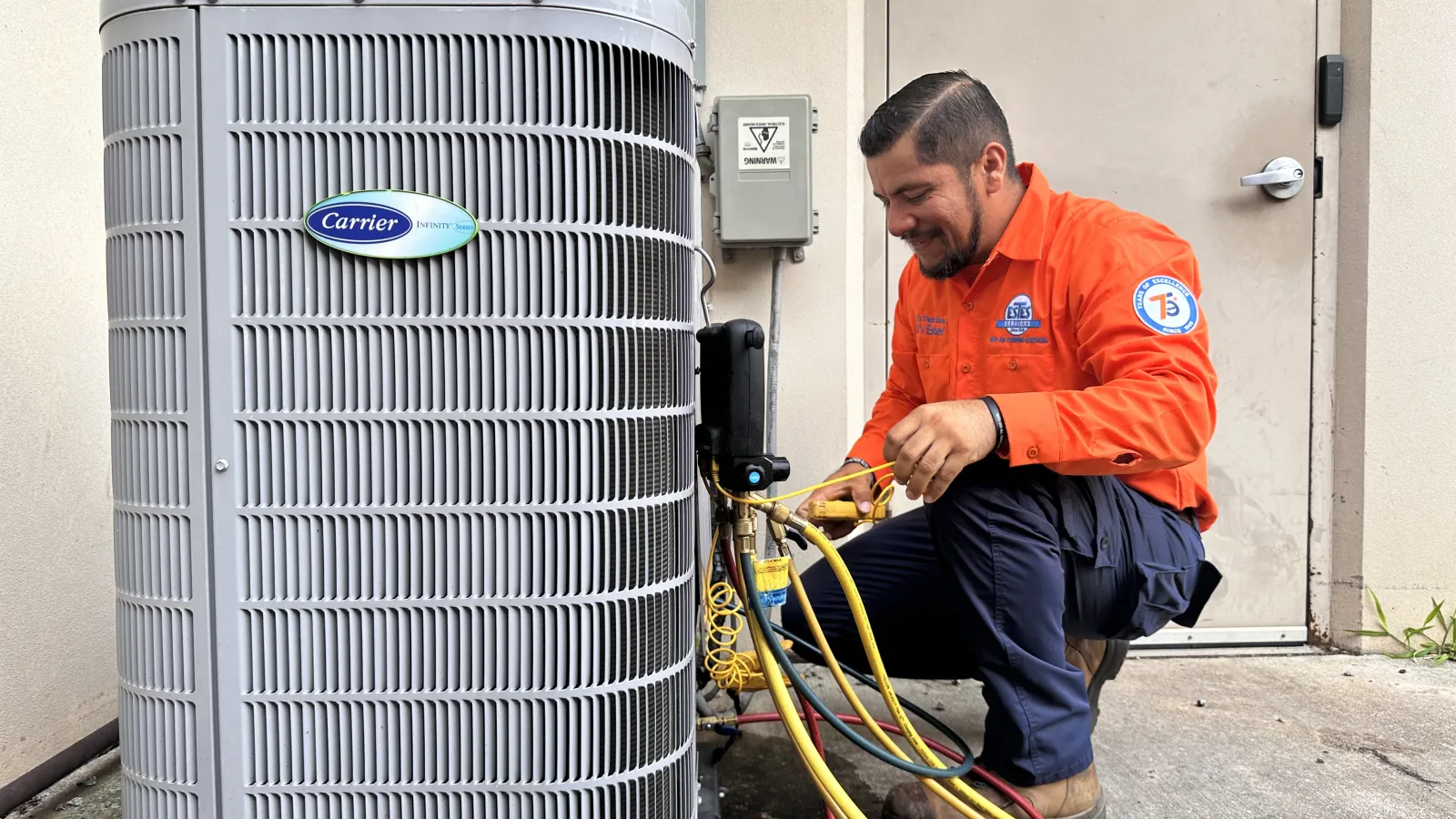 Technician in Estes Services uniform servicing a Carrier heat pump unit outdoors with diagnostic hoses attached