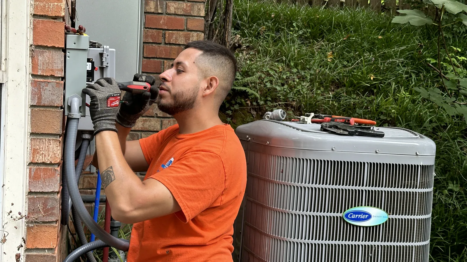 Estes professional installer working on a panel next to Carrier HVAC unit by brick wall.