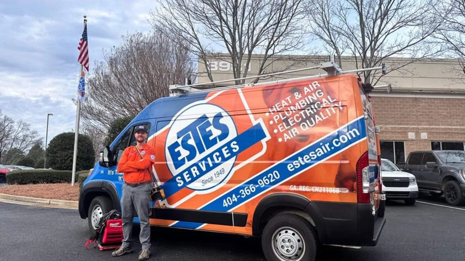 Estes Services HVAC and plumbing work van with technician standing beside it under an overcast sky in a parking lot.
