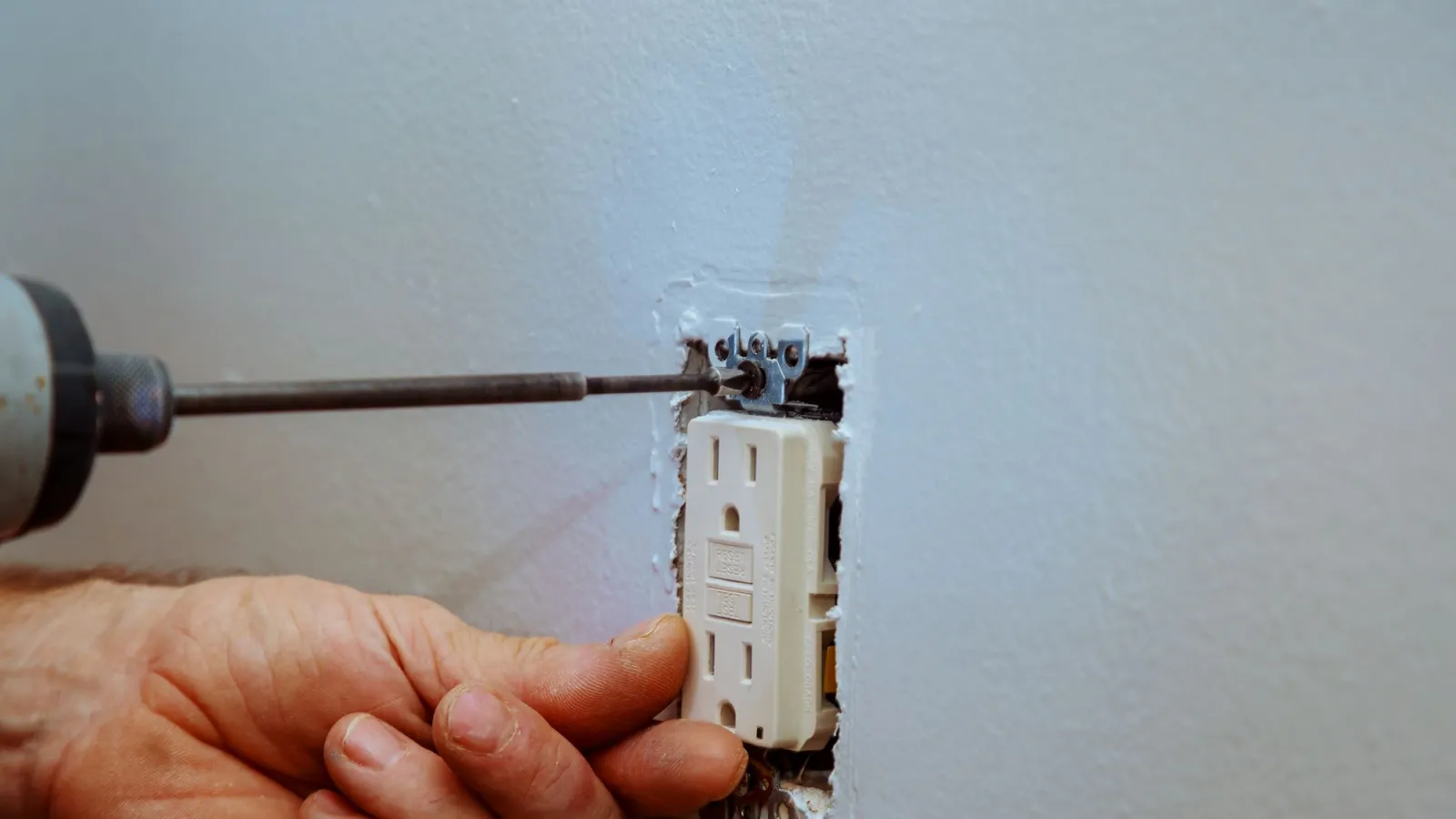 Estes Electrician checking a not working nstalling a white electrical outlet into a wall using a screwdriver for home wiring repair.