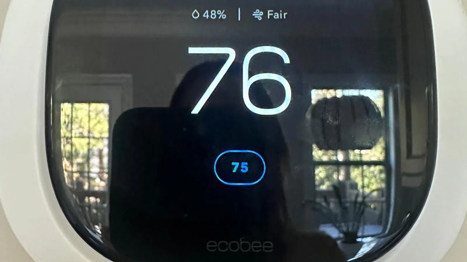 Smart thermostat displaying temperature 76°F with humidity 48% and air quality fair on black screen.