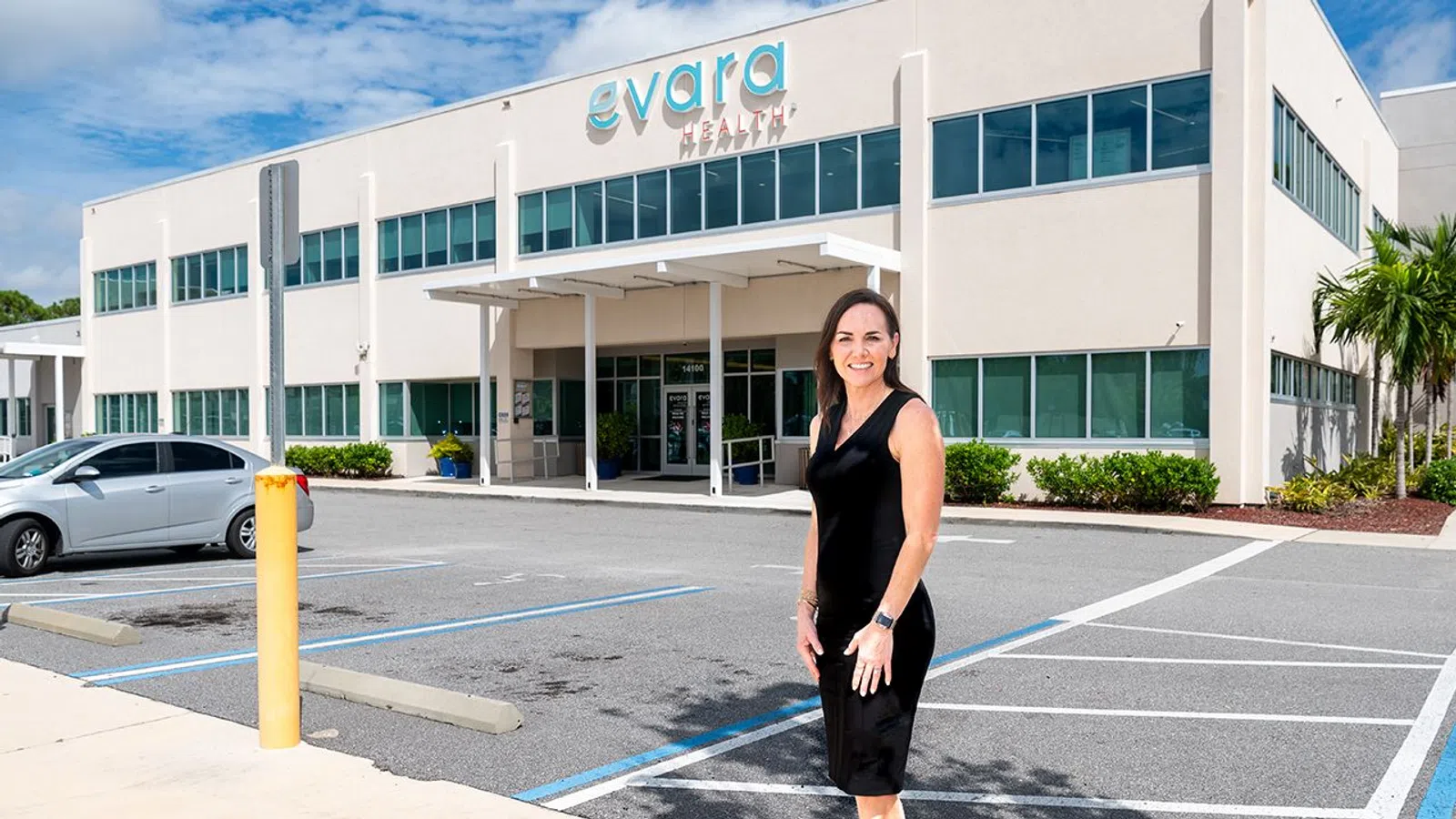 Woman in black dress standing in front of Evara Health building with clear blue sky above.