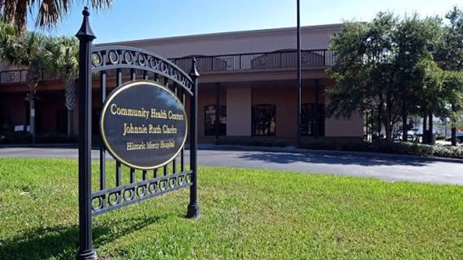 Community Health Center with a black and gold sign on a green lawn in front of a two-story building under blue sky.