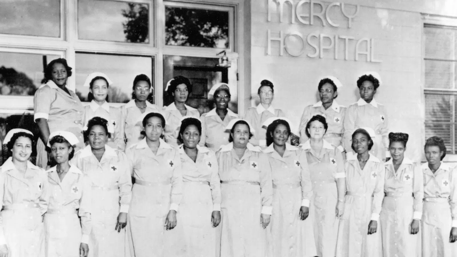 Historic black and white photo of African American nurses posing in front of Mercy Hospital building.