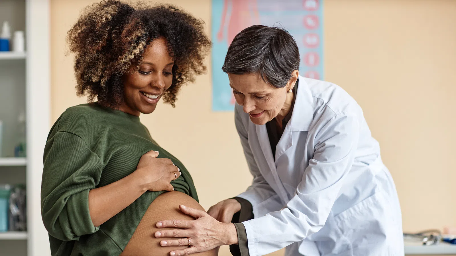 Pregnant woman smiling while doctor examines her baby bump during a prenatal checkup in clinic.