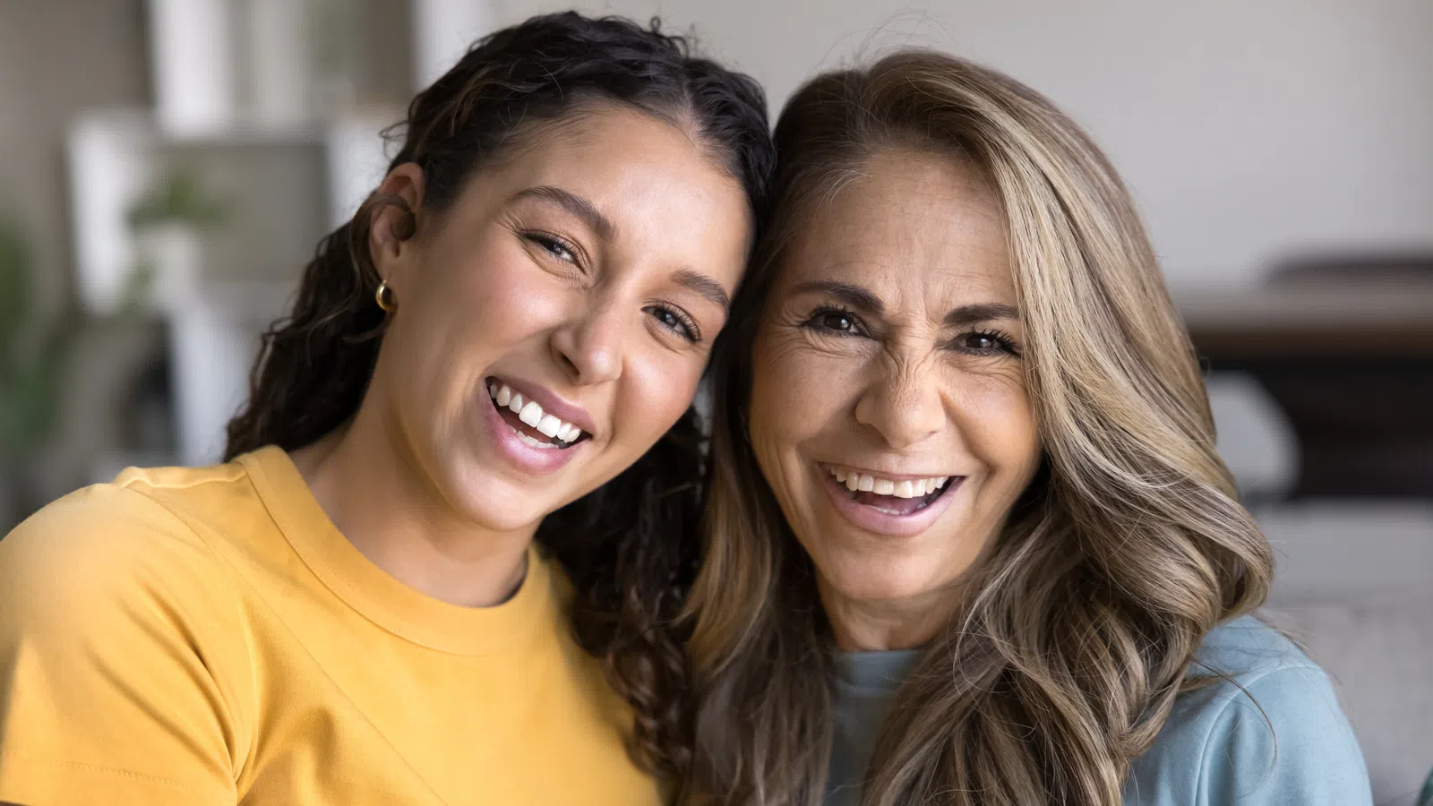 Smiling middle-aged woman and young woman hugging indoors, showing affection and happiness together.
