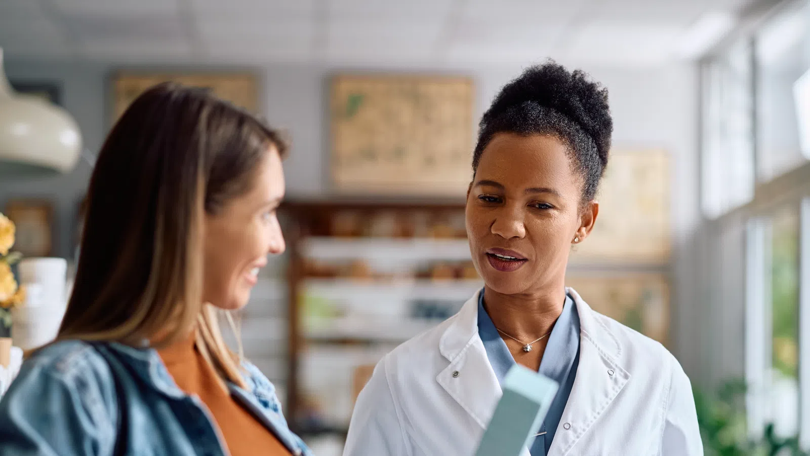 Pregnant woman consulting with female doctor in white coat about product or medication in bright clinic.