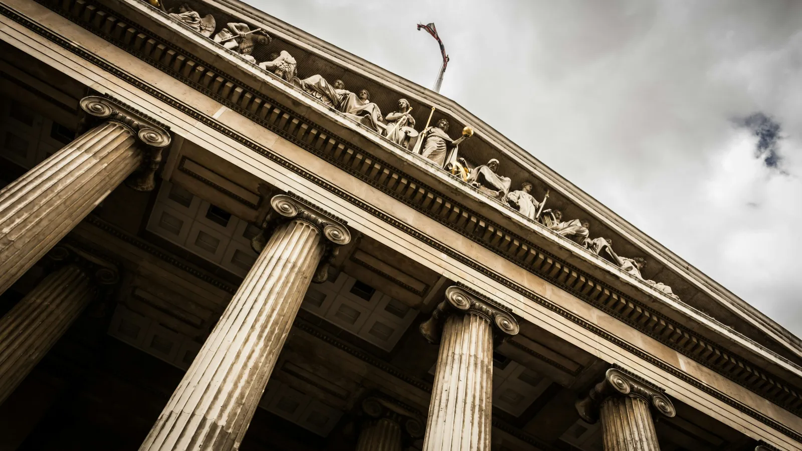 Low angle view of classical courthouse with tall columns and sculpted figures under cloudy sky.