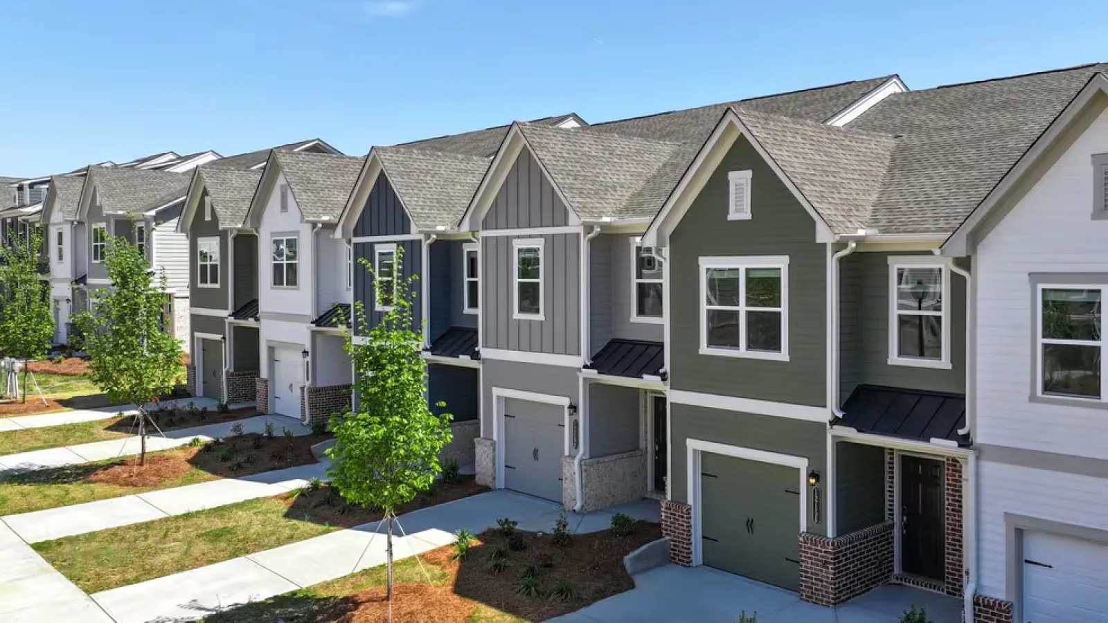 Row of modern suburban townhouses with garages, neatly landscaped yards, and clear blue sky above.
