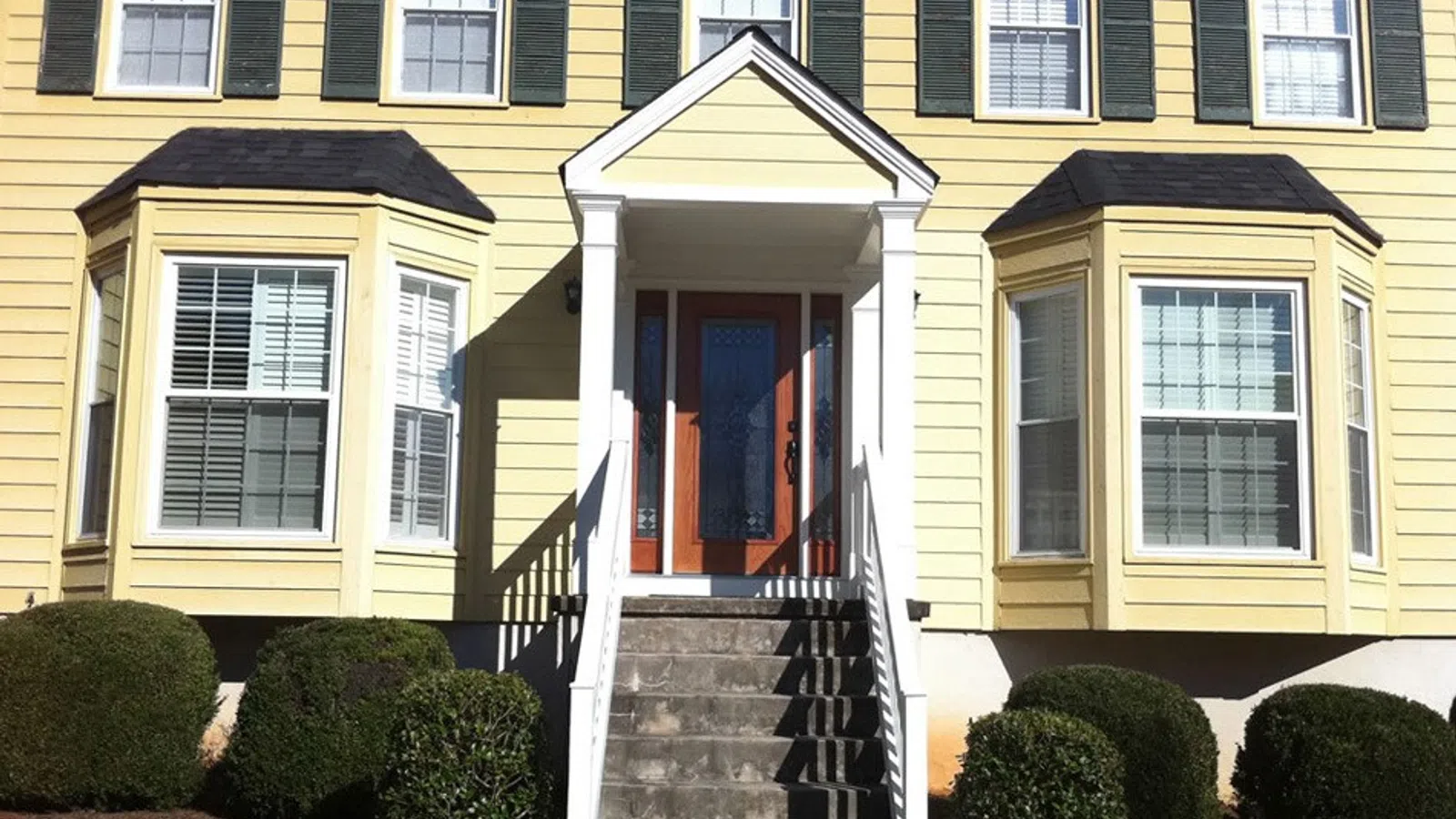 Charming yellow house with bay windows and a welcoming front porch entryway.