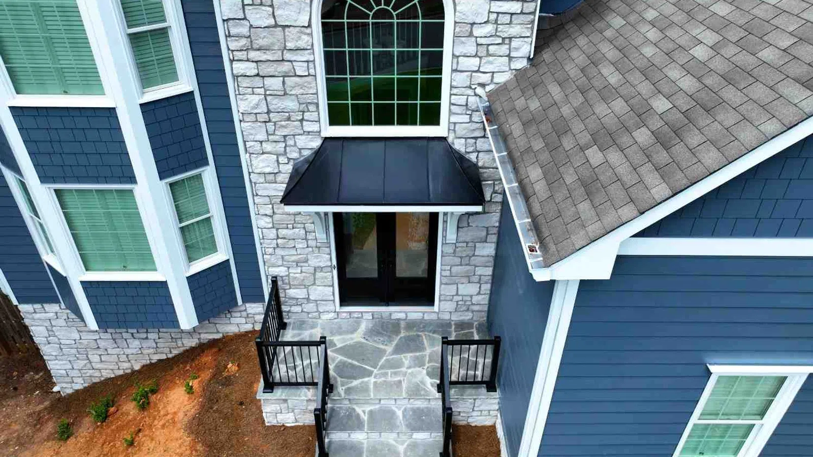Front entrance of a blue house with stone facade, large arched window, and black metal awning above door.