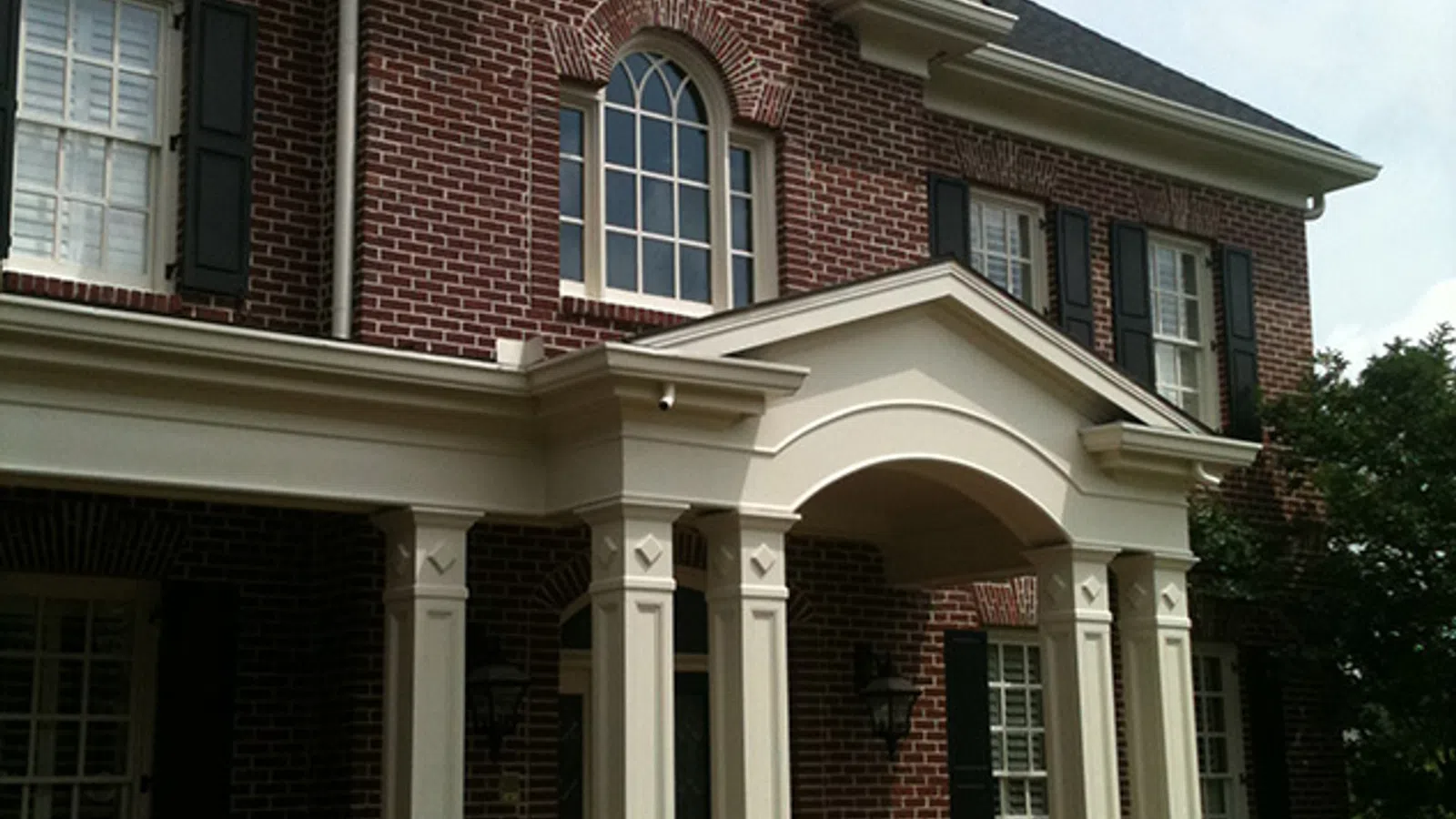 Elegant brick house with a white portico and classic windows, surrounded by lush greenery.