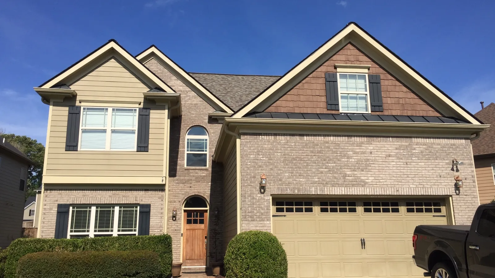 Modern two-story house with beige brick exterior, double garage, manicured lawn, and clear blue sky.
