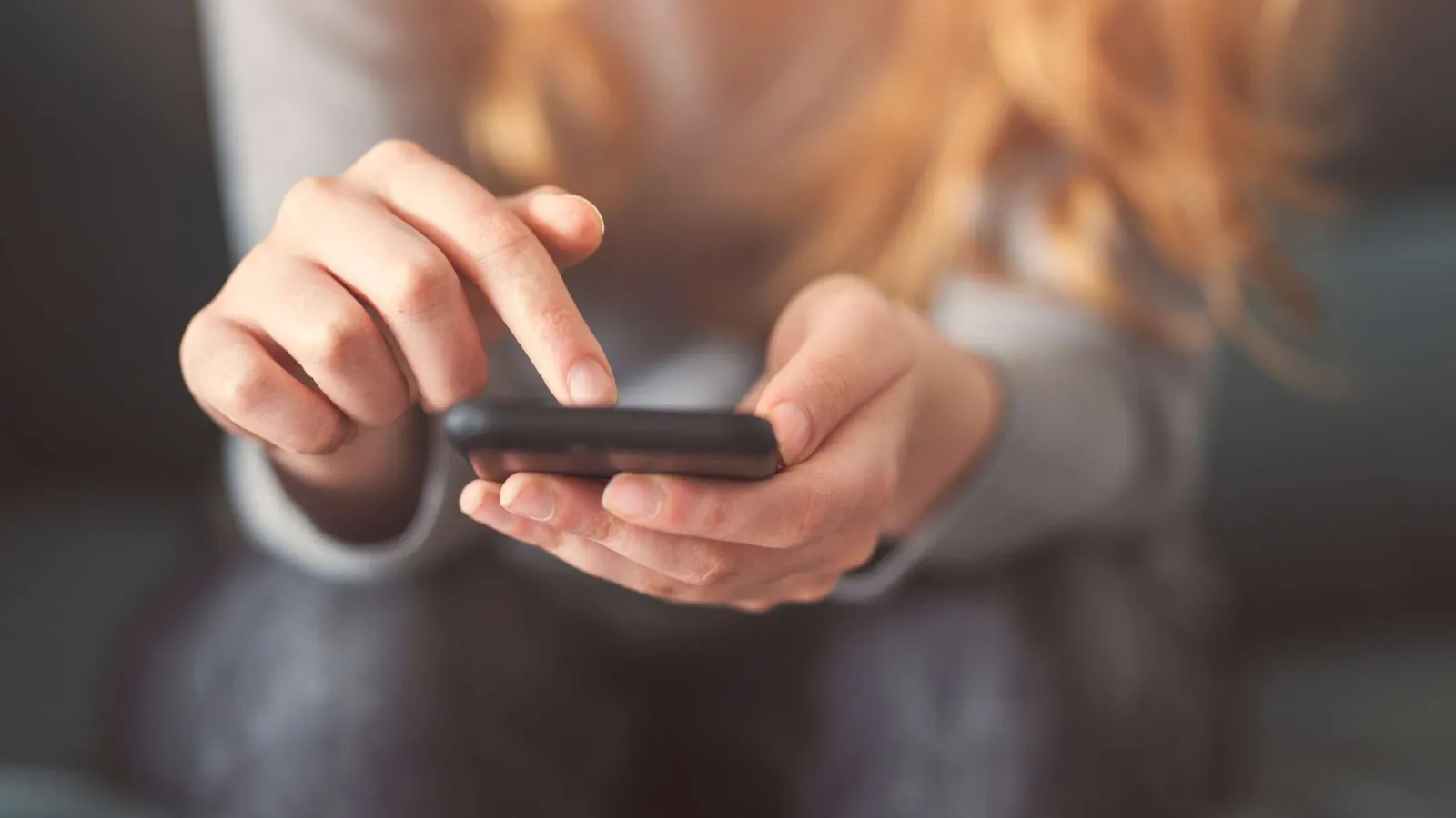 Close-up of person using smartphone with finger tapping screen, blurred background, natural light.