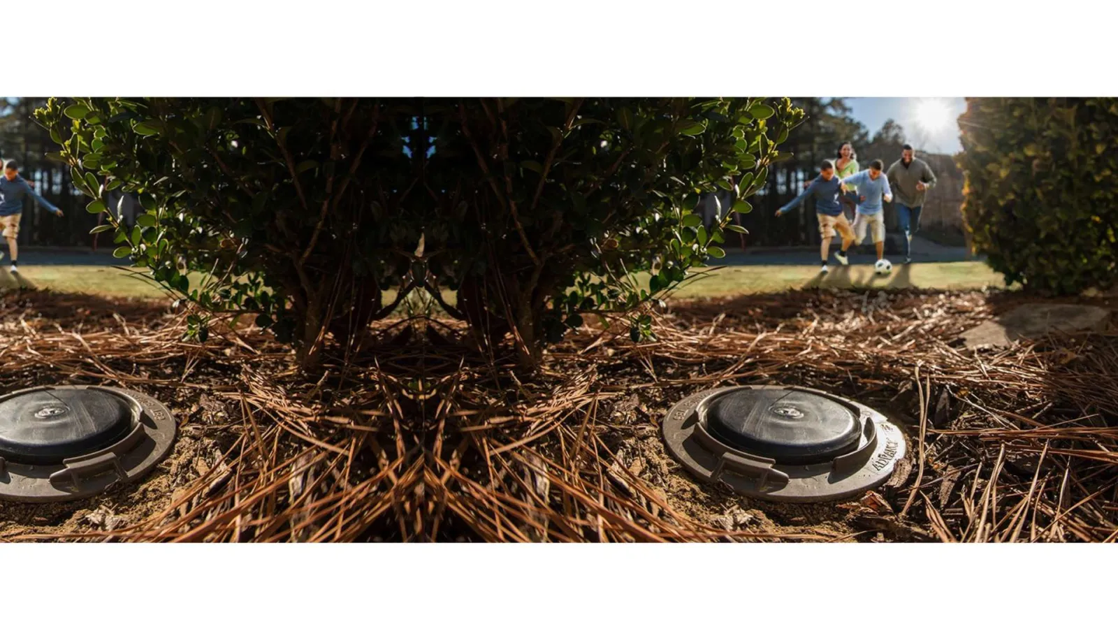 Close-up of a sprinkler head in a garden with kids playing soccer in the blurred background on a sunny day.