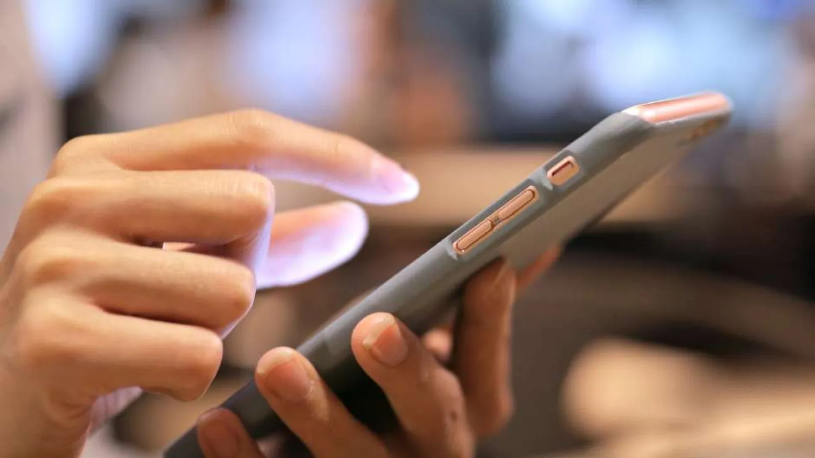 Person using a smartphone with a protective case, tapping the screen indoors with blurred background