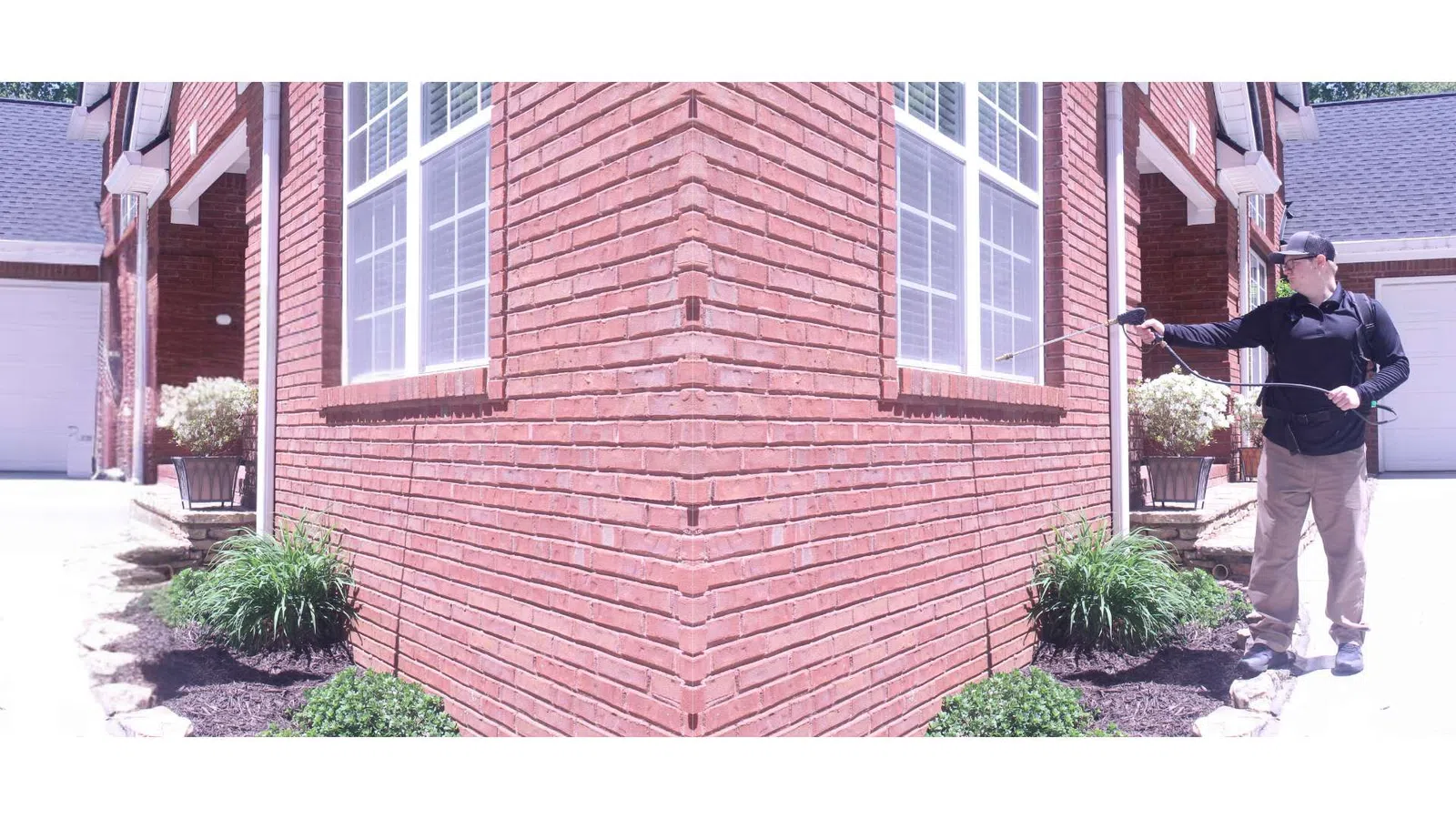 Person spraying pesticide around the foundation of a red brick house near garden plants on a sunny day
