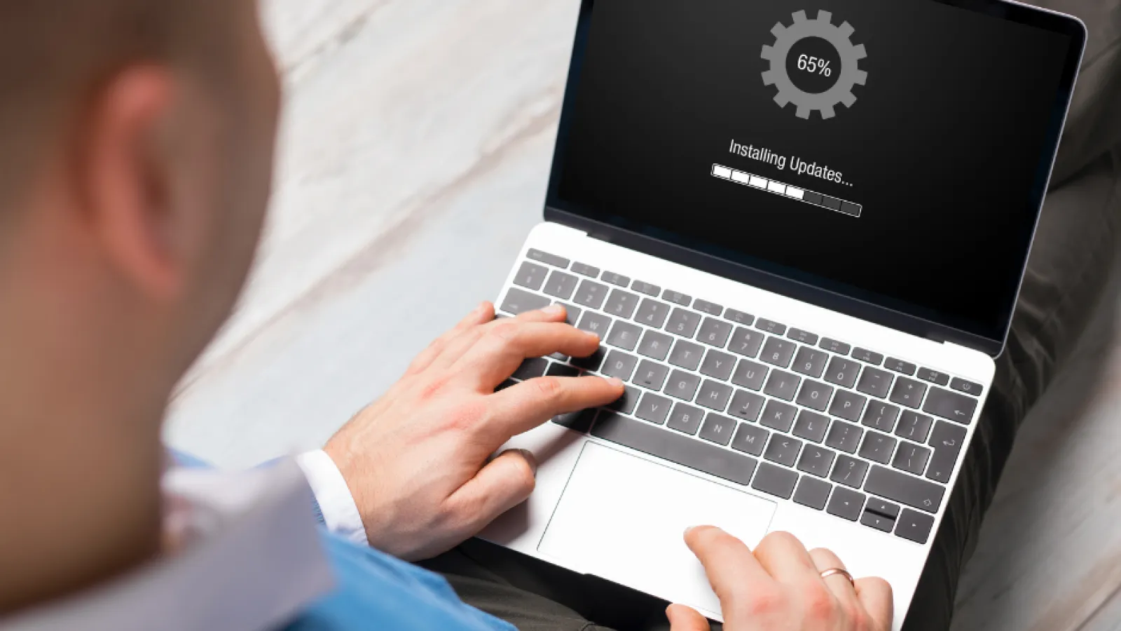 Man using laptop with screen showing 65% progress installing software updates