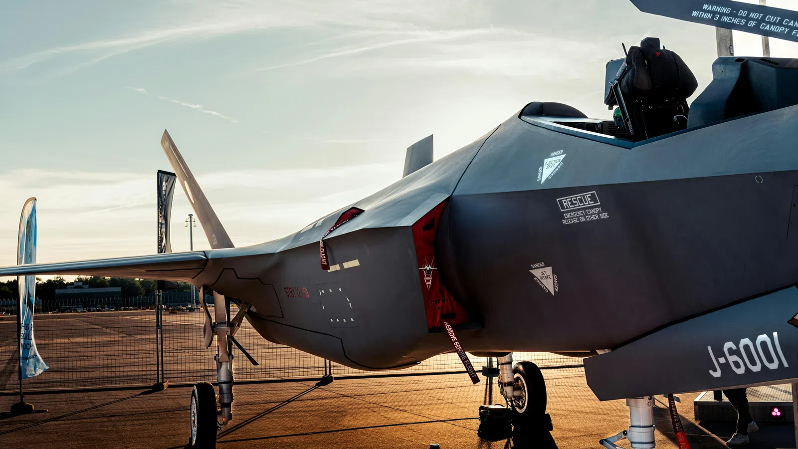 Military stealth fighter jet parked on runway at sunset with detailed fuselage and cockpit view