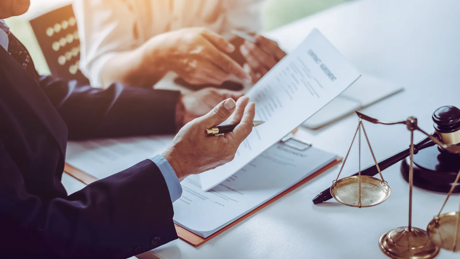 Lawyer discussing legal contracts with client at desk featuring scales of justice and gavel