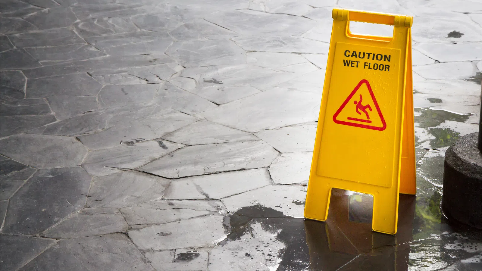 Yellow caution sign on wet stone floor warning of slippery surface and wet floor hazard.