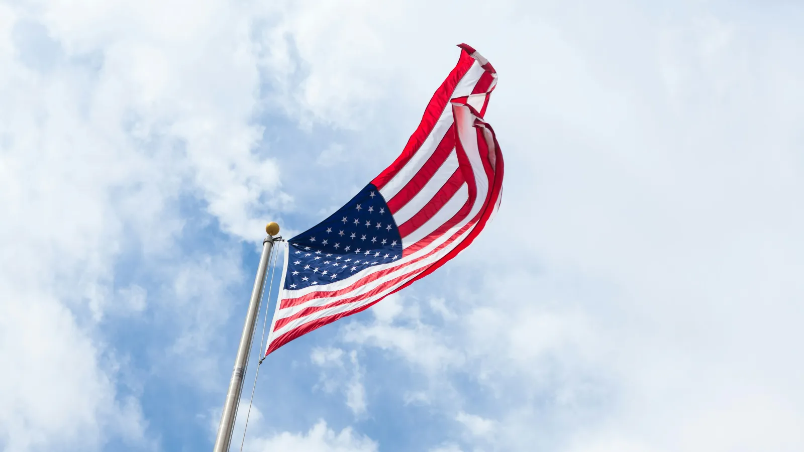 Waving American flag against a blue sky with white clouds.