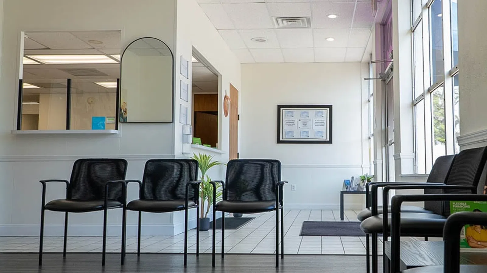 Bright and clean waiting room with black chairs, large windows, and framed certificates on the wall.