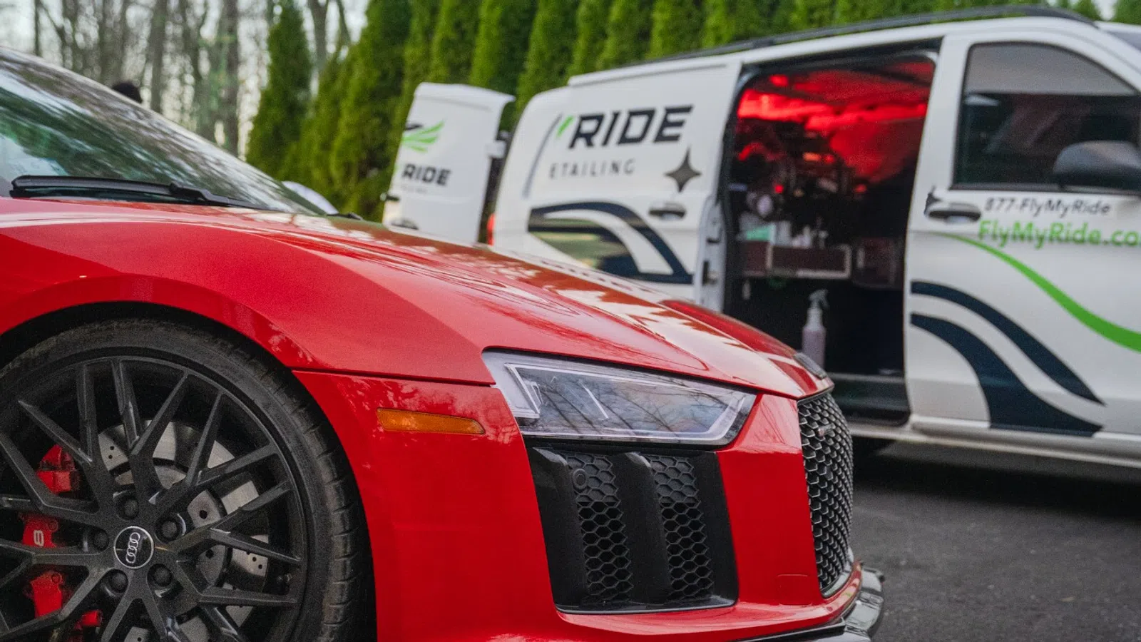Close-up of a red Audi sports car with a Ride Detailing van in the background on a paved surface.