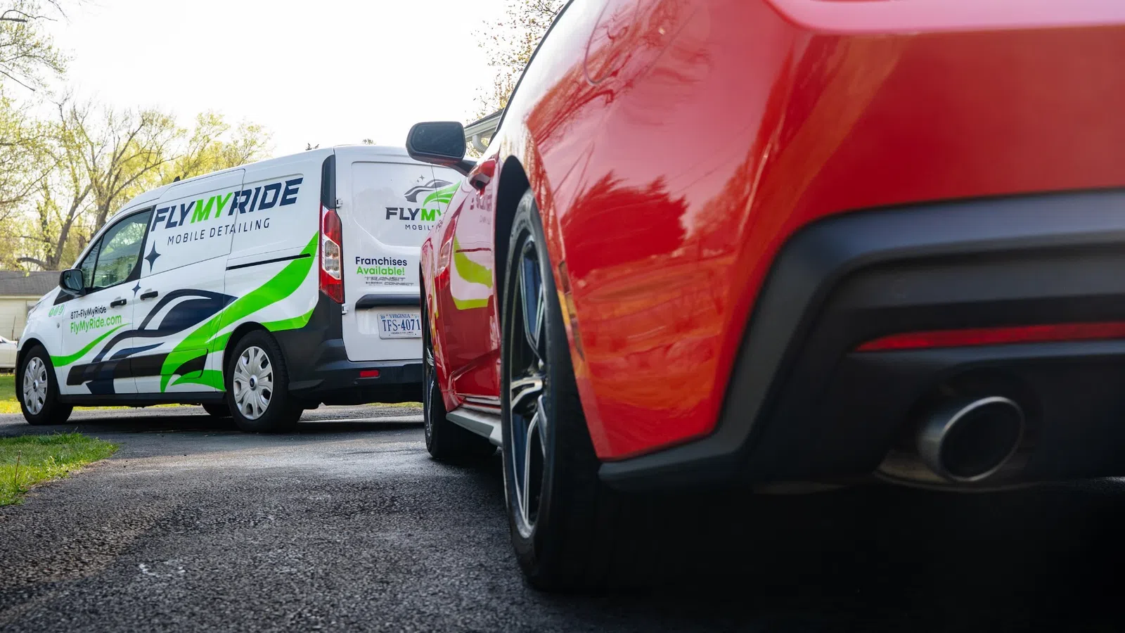 Red sports car parked near a Fly My Ride mobile detailing van in a residential driveway on a sunny day