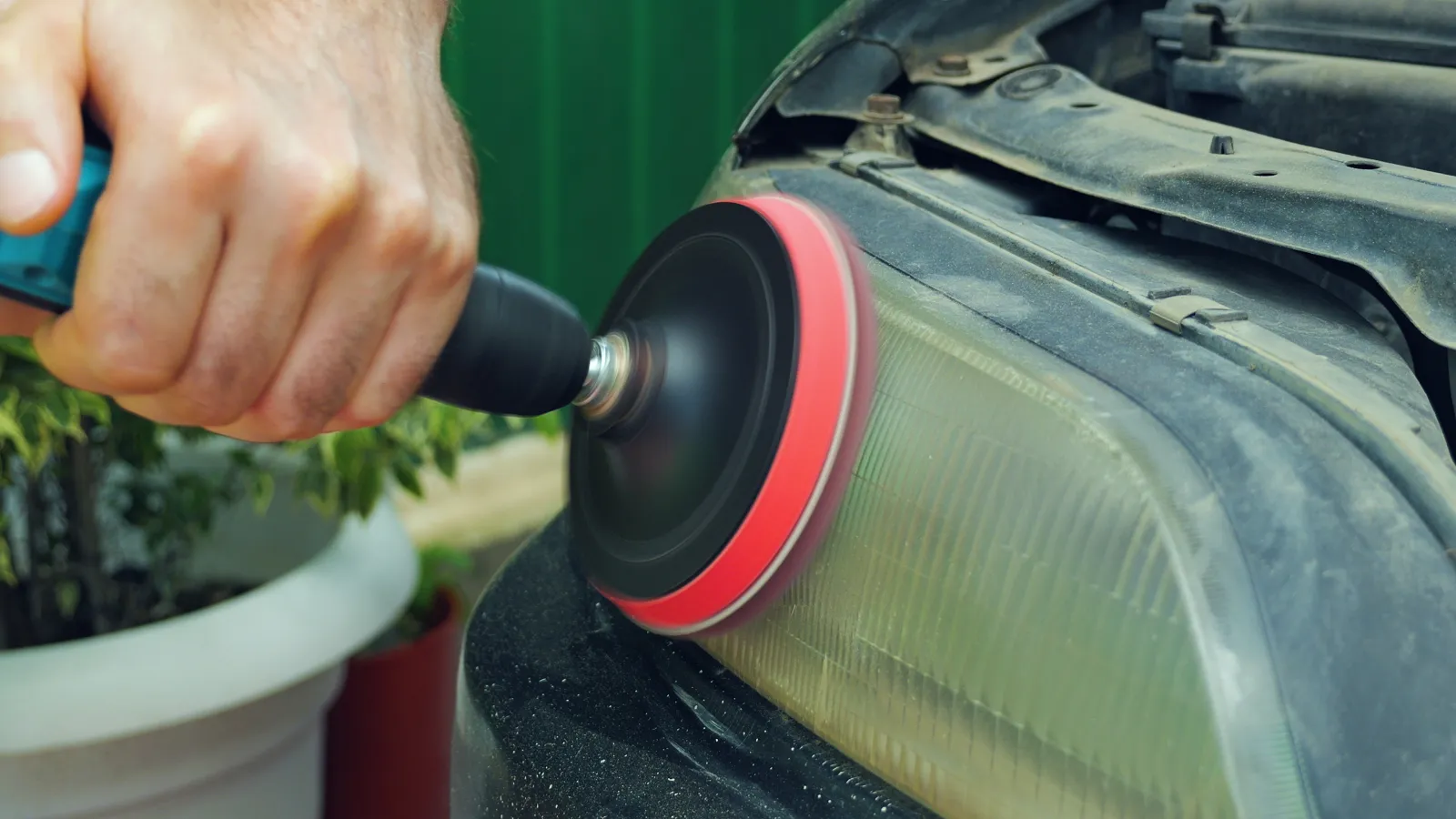 Hand polishing a car's cloudy headlight using a rotary buffer for restoration and clarity improvement.